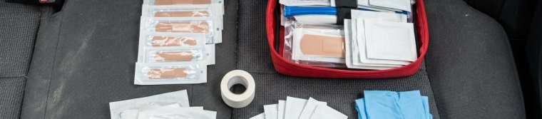 An open first aid kit on a car back seat with bandages, gauze pads, tape, antiseptic wipes, gloves and scissors