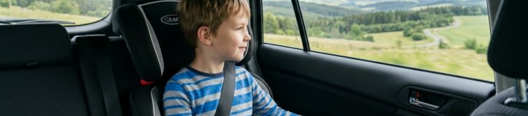 A child in a booster seat in the back seat looking out the window at distant hills
