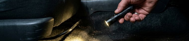Hand holding a flashlight over the carpet under a car seat.