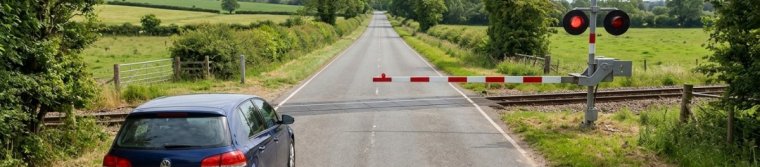A car waiting well back from a railroad crossing while the gate arm is down and the signal lights are red