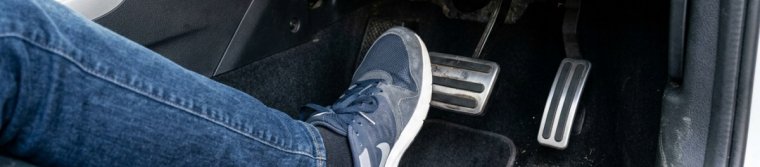 A driver's right foot pressing the brake pedal while the accelerator pedal beside it stays untouched