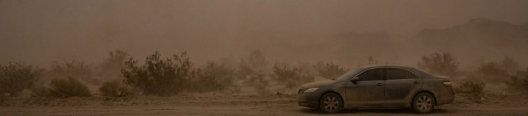 A car parked fully off a desert highway with all lights off during a dust storm
